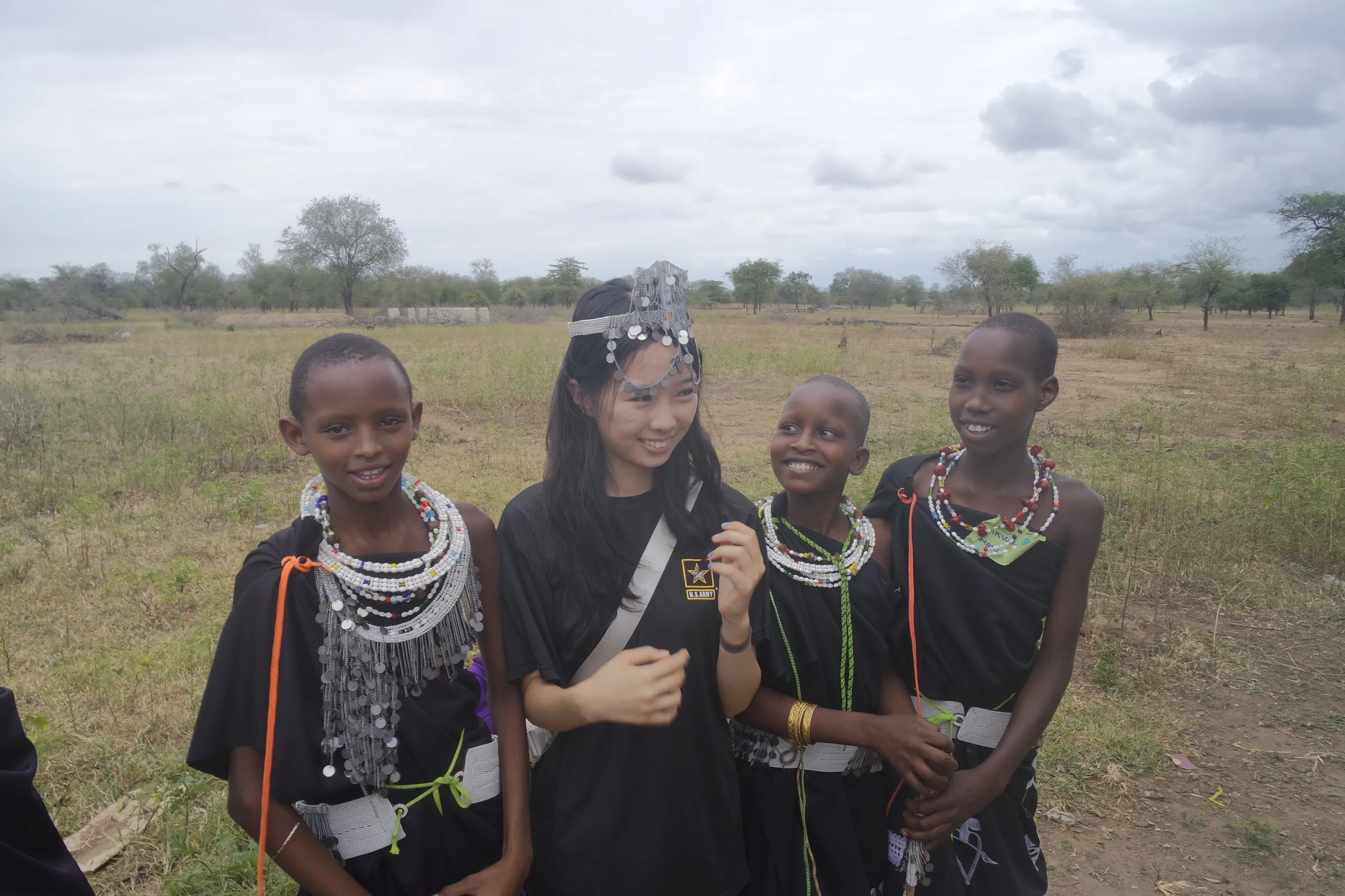 Korrine Lee in a beaded headpiece with three Maasai girls in beaded collars, standing in grassland in Tanzania