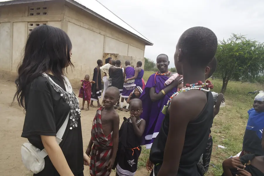 Korrine, seen from behind, with Maasai women and children outside a building