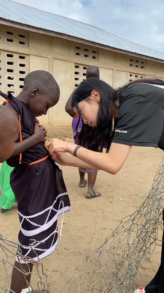 Korrine bending down to adjust a Maasai girl’s dress outside a building