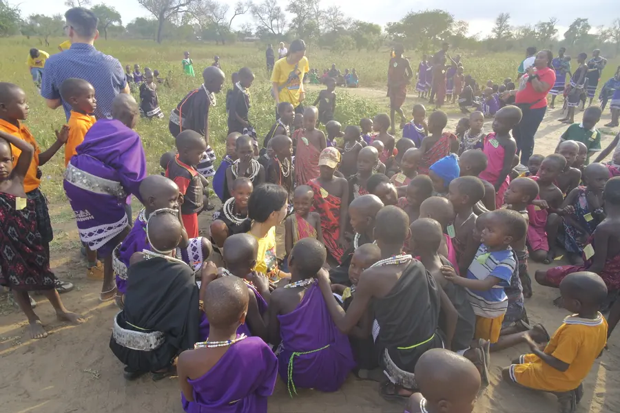 Maasai children gathered on sandy ground around volunteers