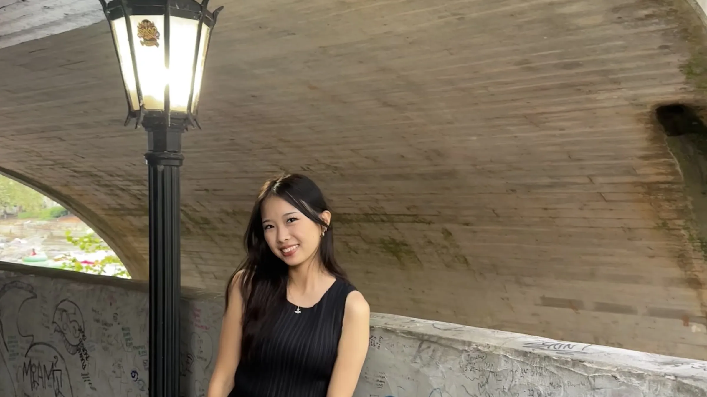 Korrine Lee leaning on a wall beside a street lamp under a stone bridge