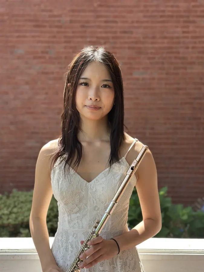 Korrine Lee in a white dress, holding a flute, in front of a brick wall