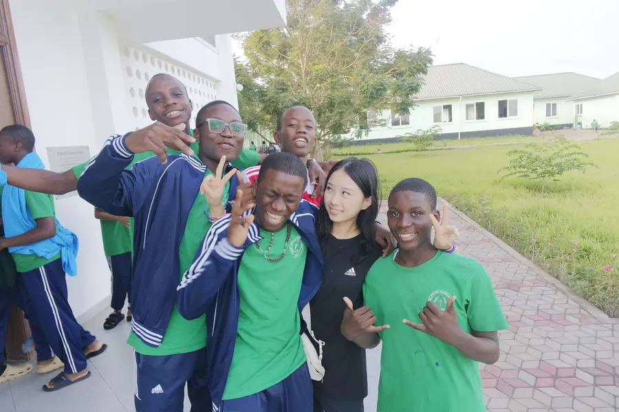 Korrine with students in green shirts and track jackets outside a school building