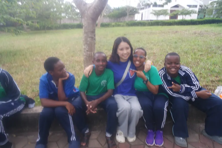 Korrine sitting on a bench with students in green uniforms