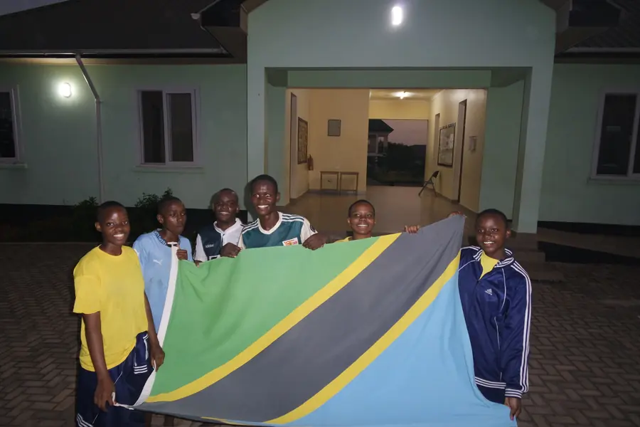 Students holding a Tanzanian flag in front of a building at night